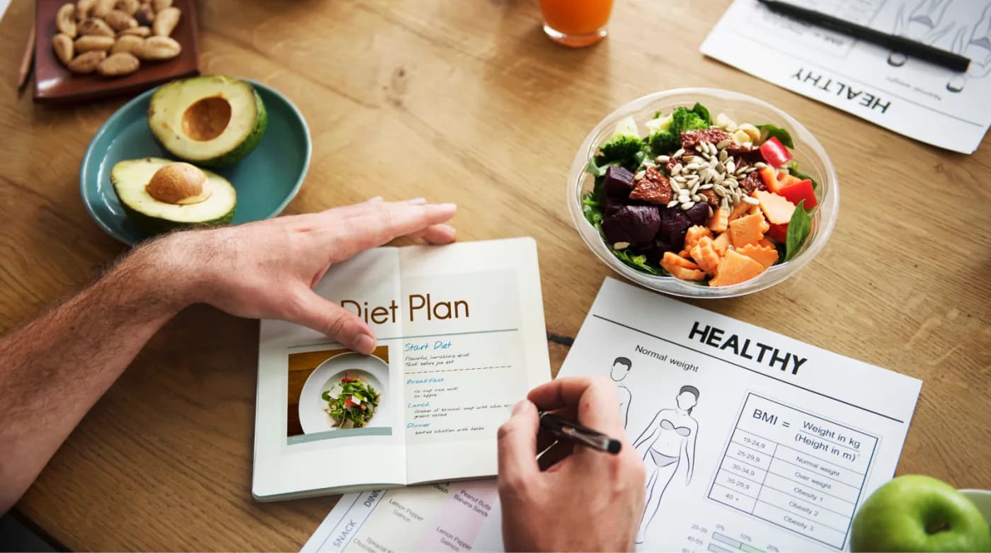 A diet plan being written at a desk beside fresh food and health charts